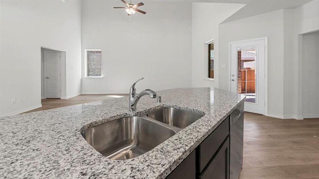 Kitchen with light stone counters, light wood-style floors, ceiling fan, stainless steel dishwasher, and a towering ceiling