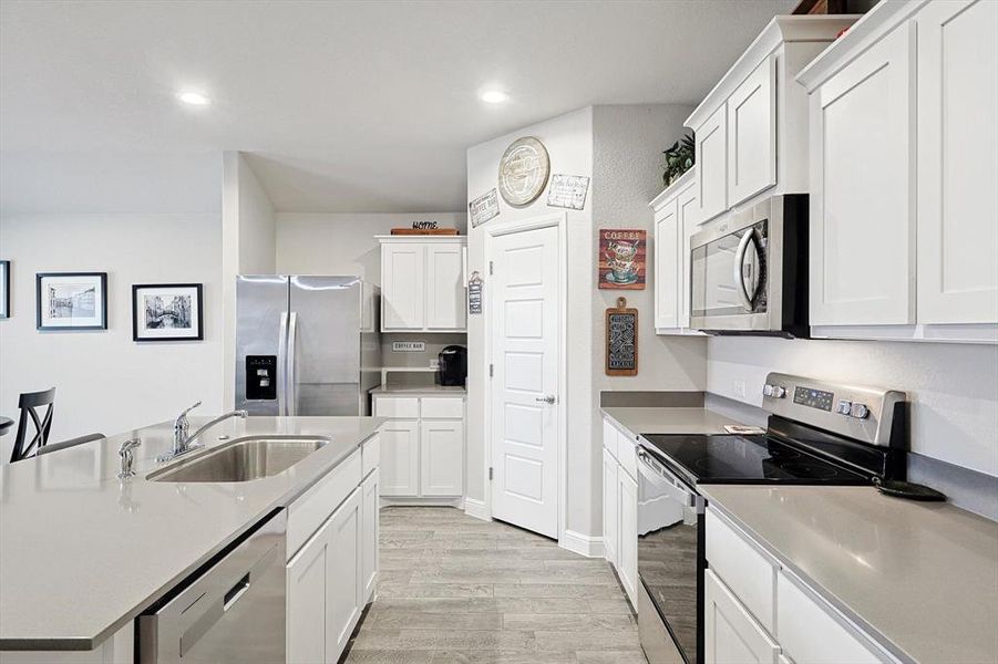 Kitchen featuring white cabinets, stainless steel appliances, light countertops, light wood-style floors, and a sink