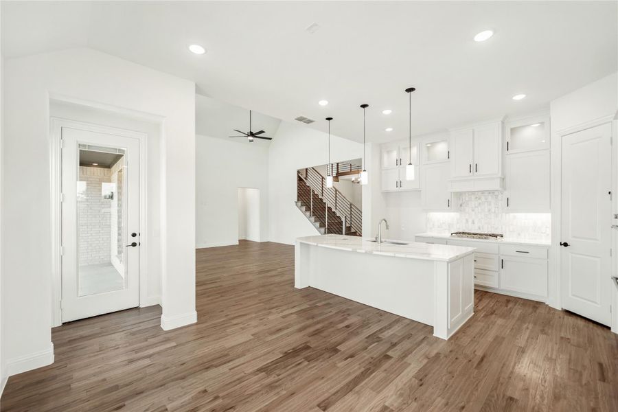Open-concept kitchen with white cabinets, large island, and hardwood floors open to living area and staircase