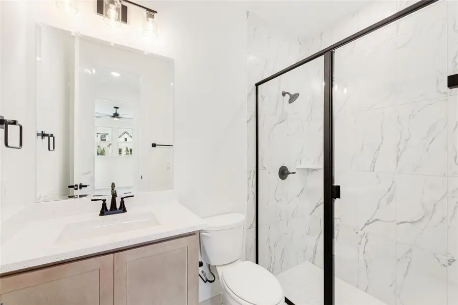 Bathroom with quartz vanity, walk-in shower with marble tile walls, and black fixtures