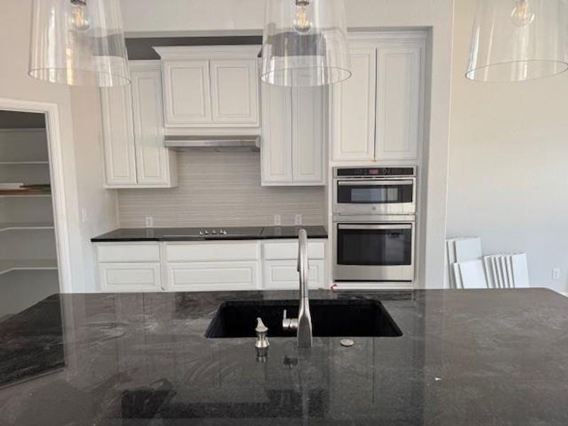 Kitchen featuring dark stone counters, white cabinetry, double oven, hanging light fixtures, and backsplash