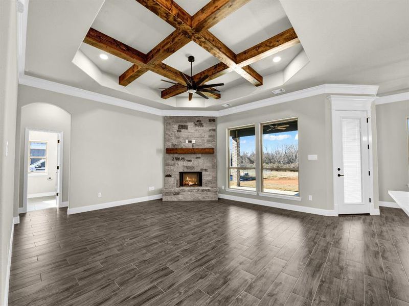 Unfurnished living room featuring a healthy amount of sunlight, a stone fireplace, coffered ceiling, and beam ceiling