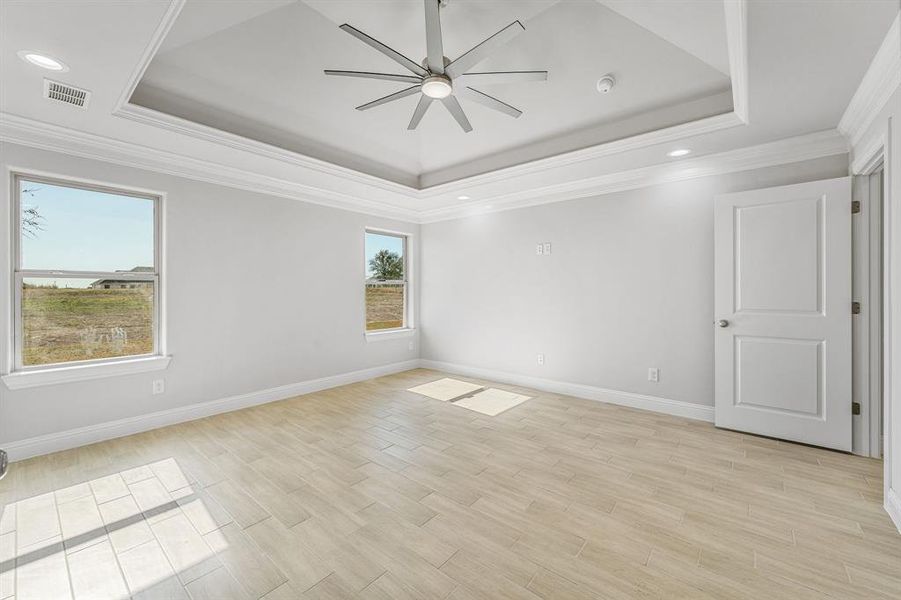 Empty room featuring a raised ceiling, ornamental molding, light wood finished floors, recessed lighting, and ceiling fan