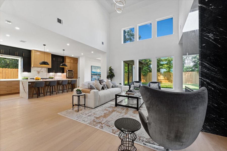 This open concept living space features high ceilings and abundant natural light from large windows. The modern kitchen has a sleek design with an island and bar seating. The living area is spacious and contemporary, and it opens to a backyard with a view of greenery. This open concept living space features high ceilings and abundant natural light from large windows. The modern kitchen has a sleek design with an island and bar seating. The living area is spacious and contemporary, and it opens to a backyard with a view of greenery.