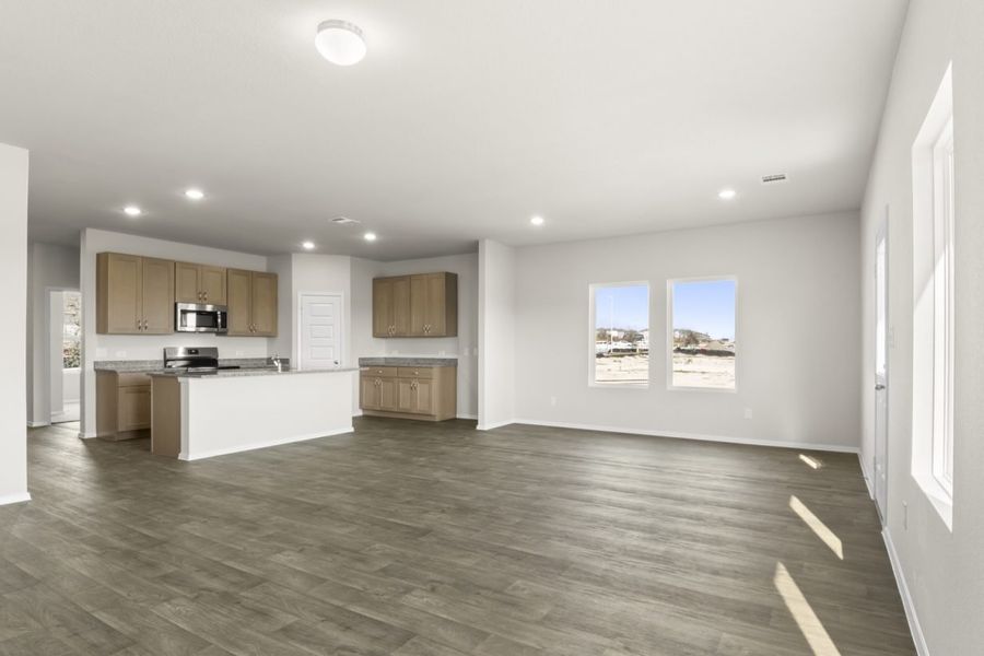 Image of a living room with light grey walls, brown vinyl flooring, and an open kitchen with a center island