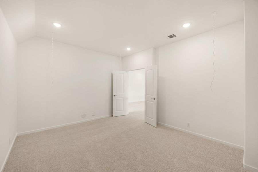 Empty bedroom with white walls, beige carpet, recessed lighting, and open double doors