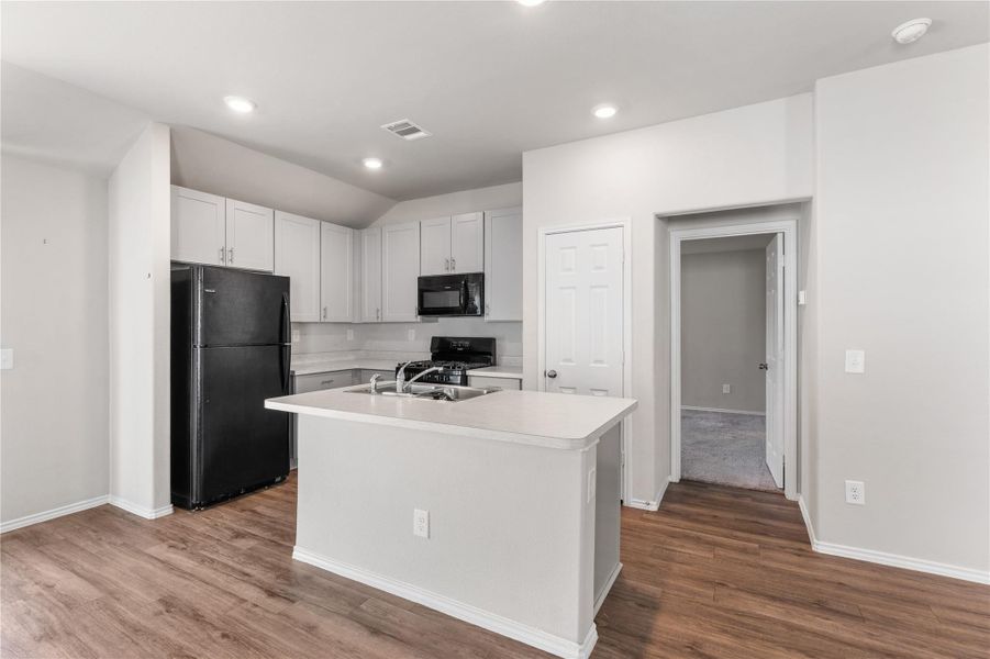 Kitchen with white cabinetry, island, and access to secondary hallway and bedroom. Kitchen with white cabinetry, island, and access to secondary hallway and bedroom.
