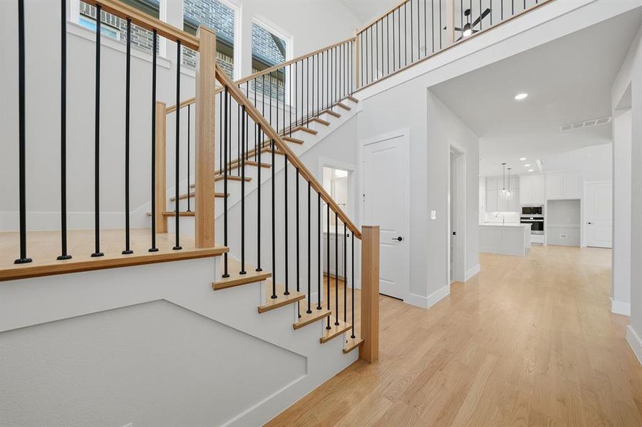 Stairs featuring wood finished floors, a towering ceiling, and recessed lighting