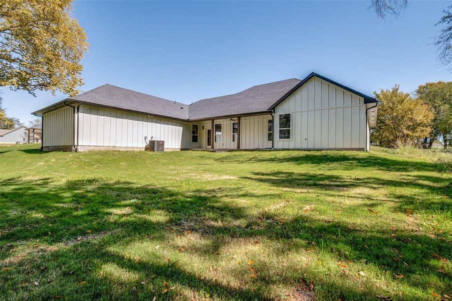 Rear view of house featuring a yard, a shingled roof, board and batten siding, and a patio Rear view of house featuring a yard, a shingled roof, board and batten siding, and a patio