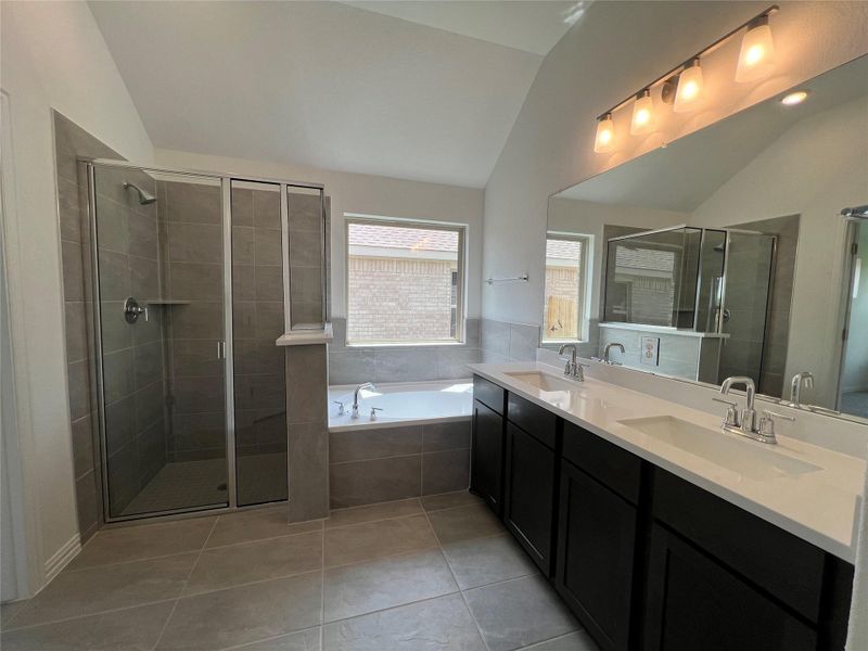 Bathroom with lofted ceiling, a garden tub, light tile patterned floors, a shower stall, and double vanity