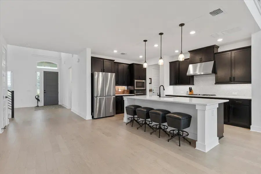 Kitchen featuring stainless steel appliances, under cabinet range hood, decorative backsplash, light countertops, and light wood-style floors