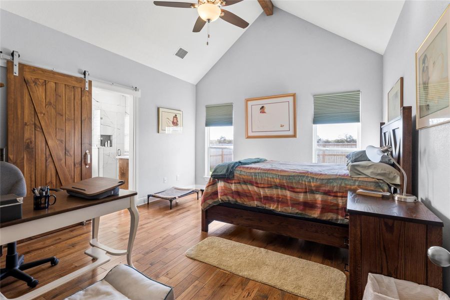 Primary Bedroom with wood flooring, a barn door, ceiling fan, ensuite bathroom.