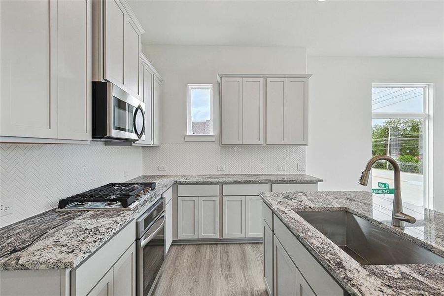 Kitchen with appliances with stainless steel finishes, light hardwood / wood-style flooring, tasteful backsplash, and sink