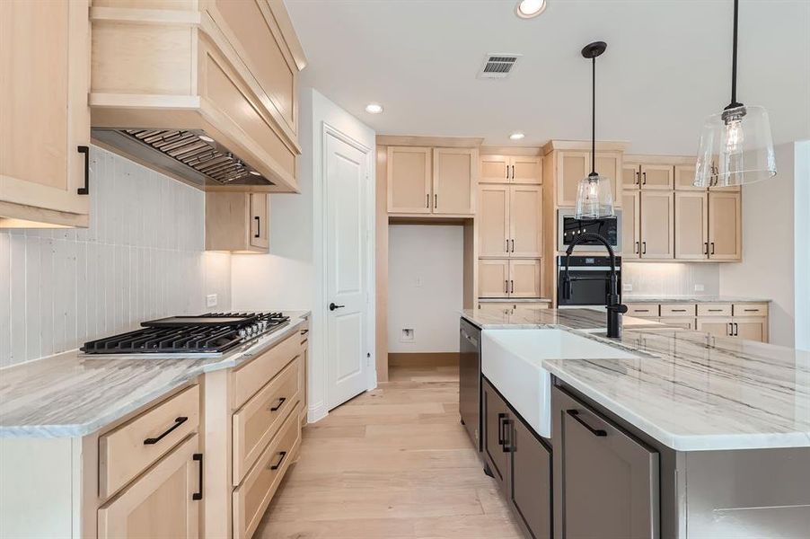 Kitchen with pendant lighting, premium range hood, a kitchen island with sink, appliances with stainless steel finishes, and light wood-type flooring