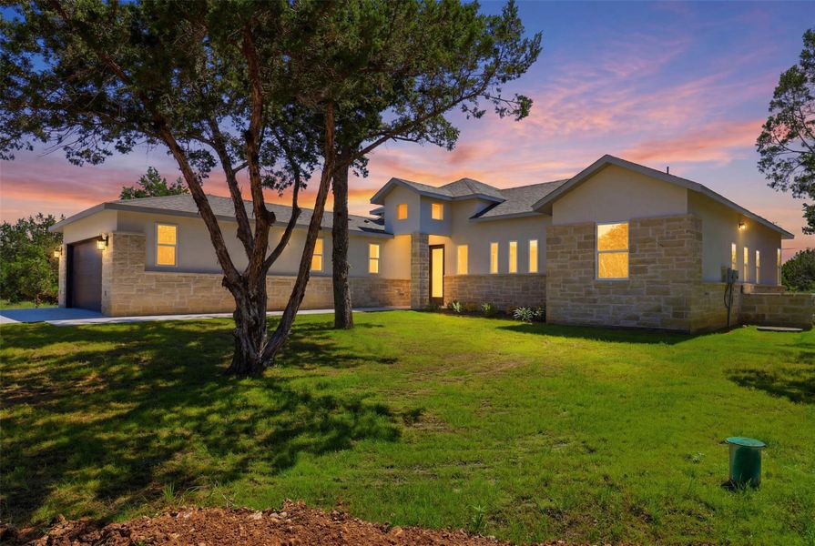 Contemporary single-story residence featuring a stucco and stone facade, an attached garage, multiple windows, a prominent entrance, and a manicured lawn Contemporary single-story residence featuring a stucco and stone facade, an attached garage, multiple windows, a prominent entrance, and a manicured lawn
