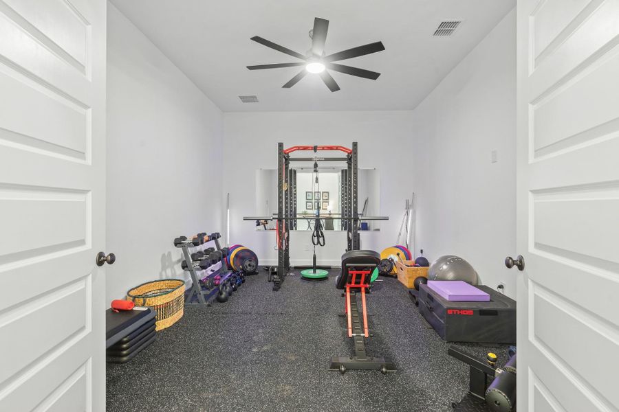 This photo showcases a well-equipped home gym in the game room/flex room.  With double doors and a multi-blade ceiling fan to complete the aesthetics.