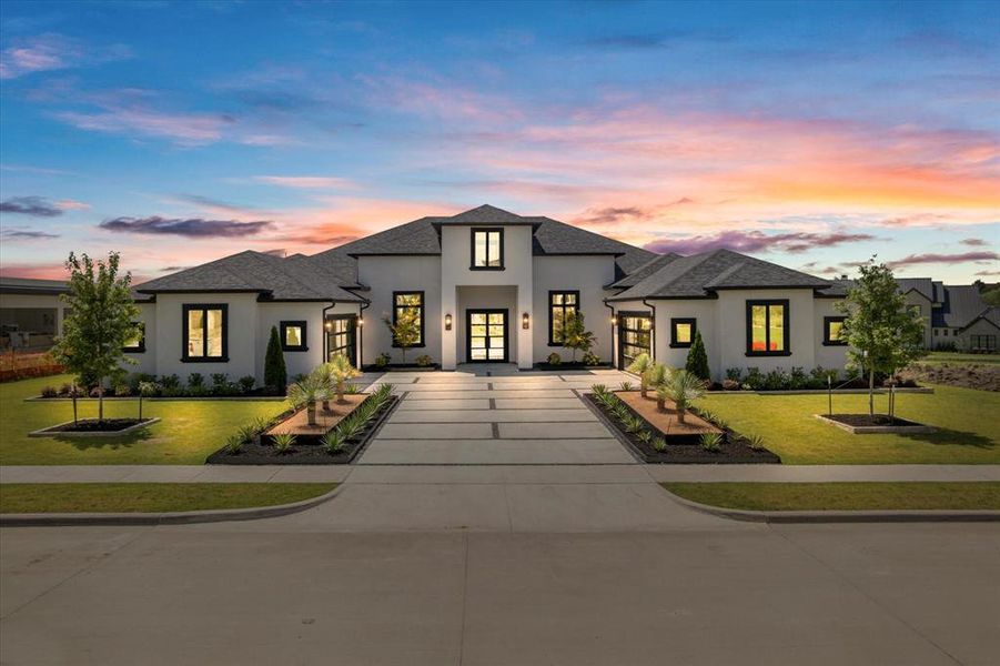 View of front facade with stucco siding, french doors, a lawn, and curved driveway
