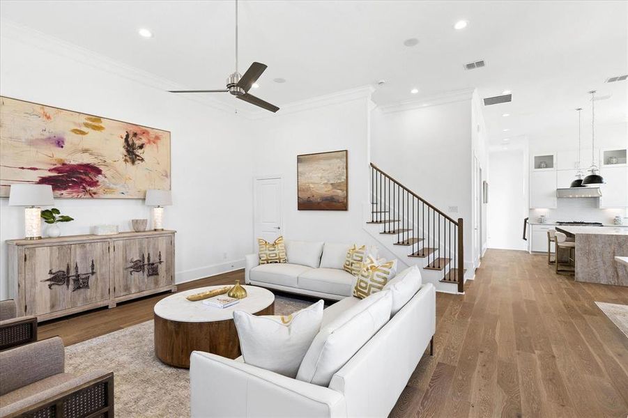 Open-concept living space featuring wide-plank wood-finish flooring, a contemporary ceiling fan, recessed lighting, and crown molding