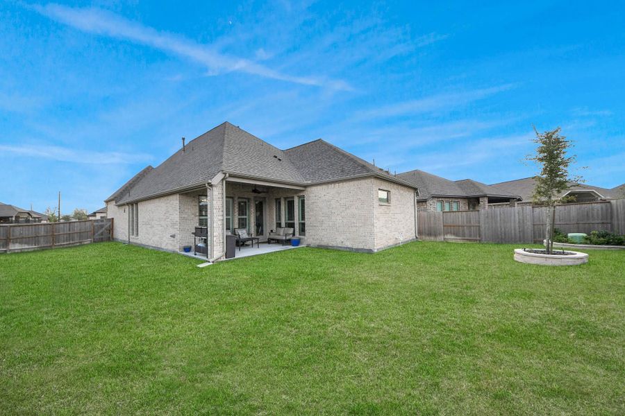 This photo features a modern brick house with a spacious, well-maintained backyard. There's a covered patio area, perfect for outdoor seating, and a wooden fence surrounds the property for privacy. Ideal for family gatherings and relaxation.