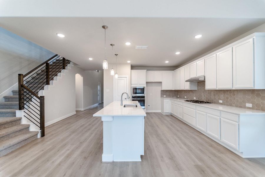 Kitchen featuring white cabinets, an island with sink, light stone countertops, arched walkways, and light wood-style flooring