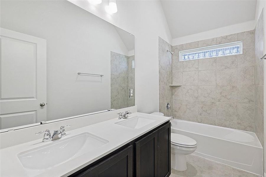 Full bathroom with tile patterned floors, vaulted ceiling, toilet, vanity, and tiled shower / bath