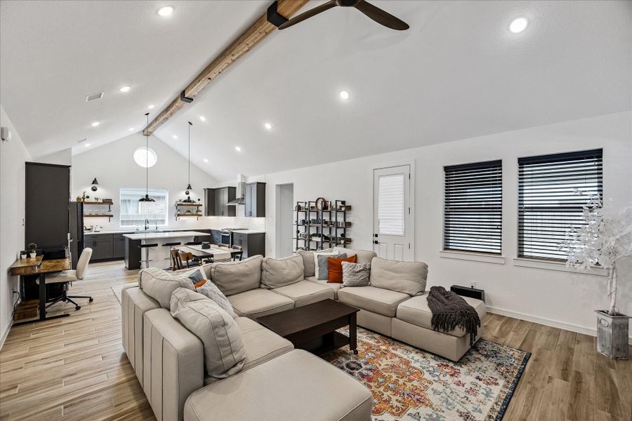 Expansive open-concept living area featuring vaulted ceilings, exposed wood beam detail, recessed lighting, and seamless flow into the kitchen and dining spaces.