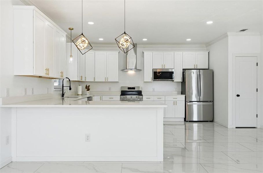 Kitchen featuring stainless steel appliances, white cabinetry, wall chimney range hood, hanging light fixtures, and ornamental molding Kitchen featuring stainless steel appliances, white cabinetry, wall chimney range hood, hanging light fixtures, and ornamental molding