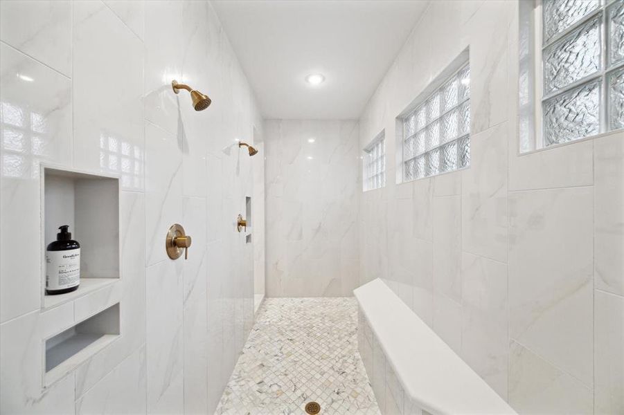 Stunning double shower featuring brushed gold shower heads, with recessed shelfs for toiletries on both sides.    This large walk-in shower offers an elegant extended tile bench seat.