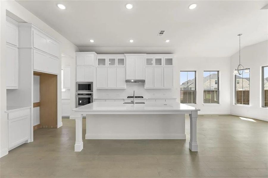 Kitchen featuring stainless steel oven, hanging light fixtures, an island with sink, built in microwave, and white cabinetry