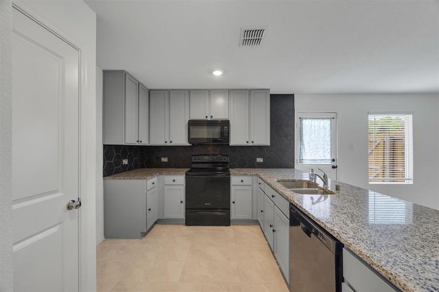 Kitchen featuring light gray cabinetry, dark hexagonal tile backsplash, granite countertops, and stainless steel dishwasher