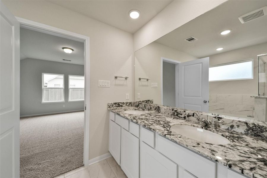 Modern en-suite featuring a dual granite vanity, ample storage, and a bright tiled shower with a privacy window.