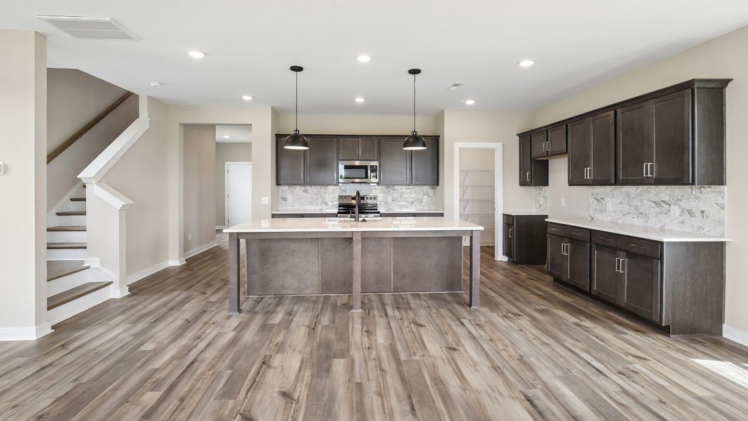 Kitchen with dark cabinetry, quartz countertops, and tile backsplash with nearby staircase
