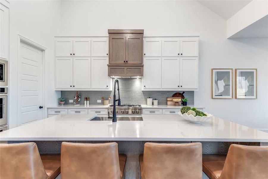 Kitchen with white cabinets, a kitchen bar, backsplash, and lofted ceiling Kitchen with white cabinets, a kitchen bar, backsplash, and lofted ceiling