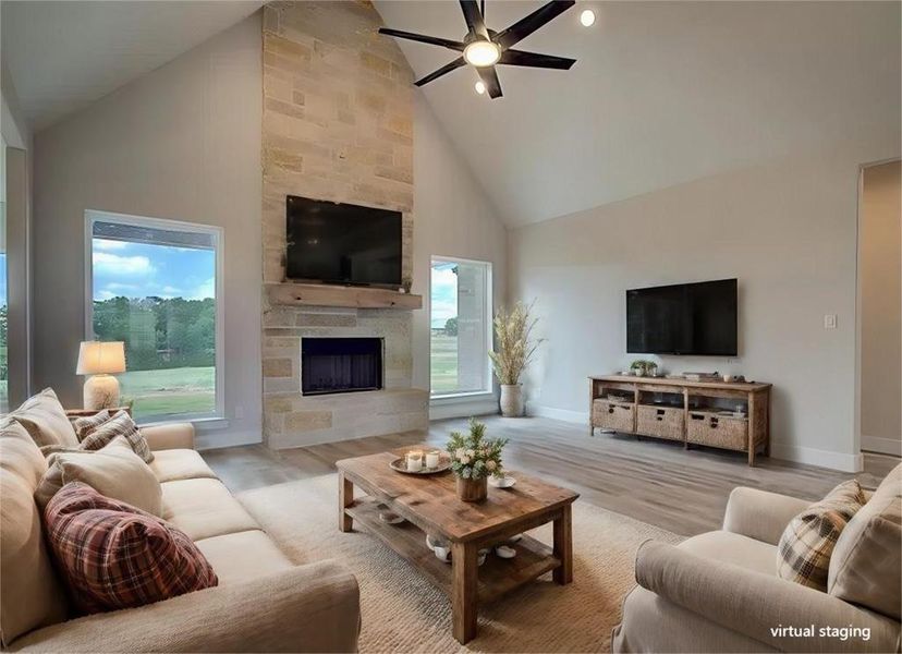 Living room featuring ceiling fan, a large fireplace, hardwood / wood-style floors, and high vaulted ceiling