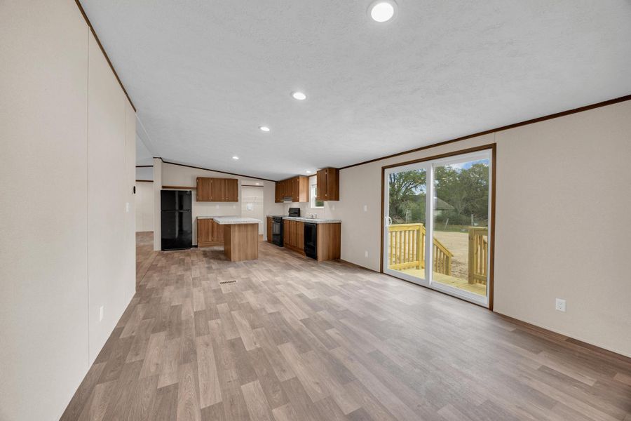 Kitchen featuring open floor plan, vaulted ceiling, light wood finished floors, brown cabinetry, and light countertops