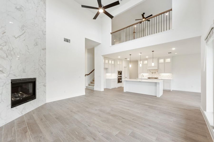 Open living area with two-story ceiling, marble fireplace, and open kitchen with white cabinets and island