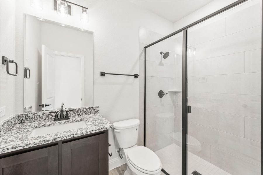 Bathroom with granite countertop vanity, glass-enclosed tile shower, and black hardware accents Bathroom with granite countertop vanity, glass-enclosed tile shower, and black hardware accents