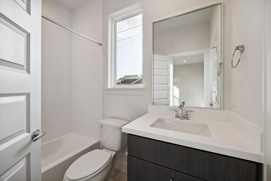 This full bathroom features a versatile shower/tub combo, perfect for relaxing baths or quick showers. The clean white subway tile adds a classic touch, while the large window brings in natural light, brightening the space. A sleek vanity with a large mirror complete the modern look.