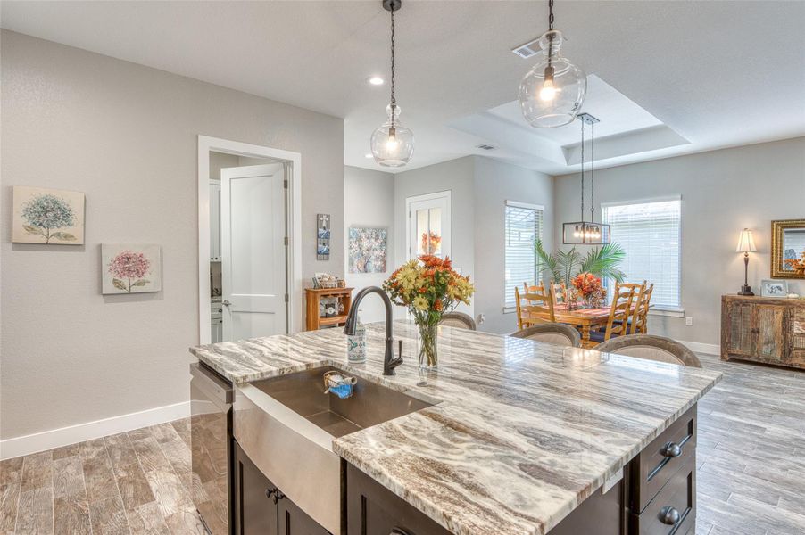 Kitchen featuring dark brown cabinets, a raised ceiling, light stone countertops, hanging light fixtures, and dishwasher