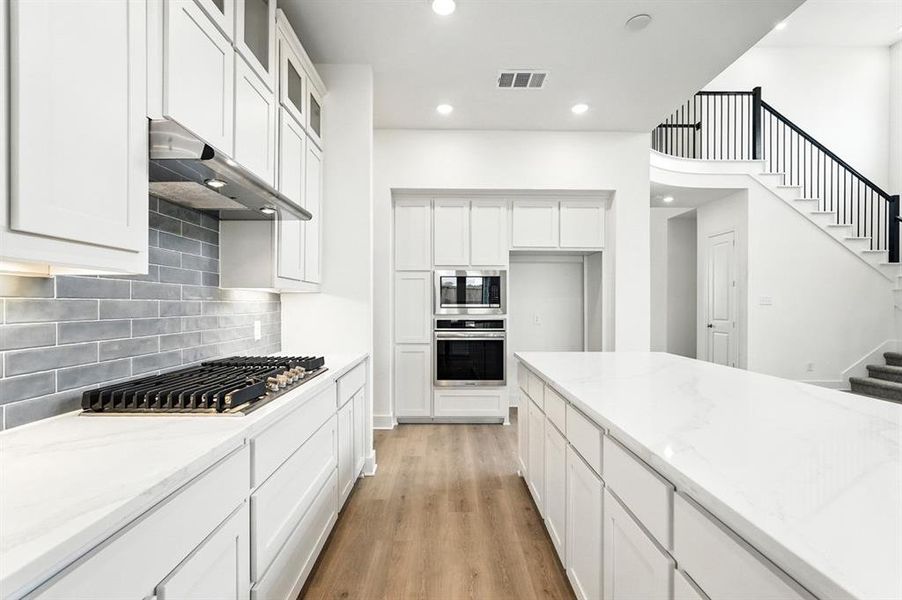 Kitchen with light wood-style floors, white cabinets, recessed lighting, appliances with stainless steel finishes, and light stone countertops Kitchen with light wood-style floors, white cabinets, recessed lighting, appliances with stainless steel finishes, and light stone countertops