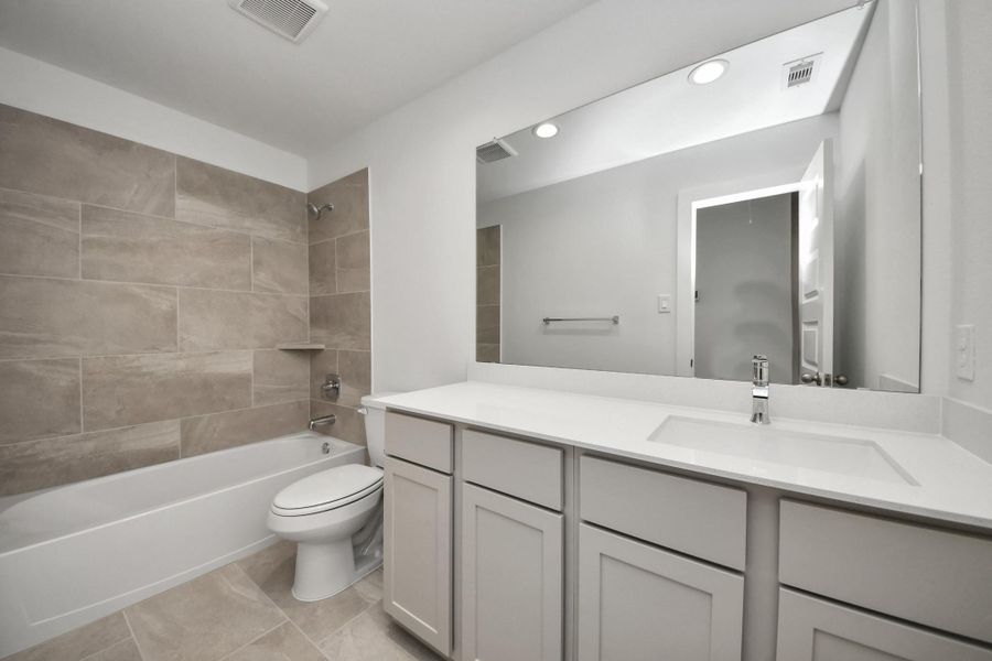 Secondary bath features tile flooring, bath/shower combo with tile surround, light stained wood cabinets, beautiful light countertop. Sample photo of completed home with similar floor plan. Actual colors and selections may vary.