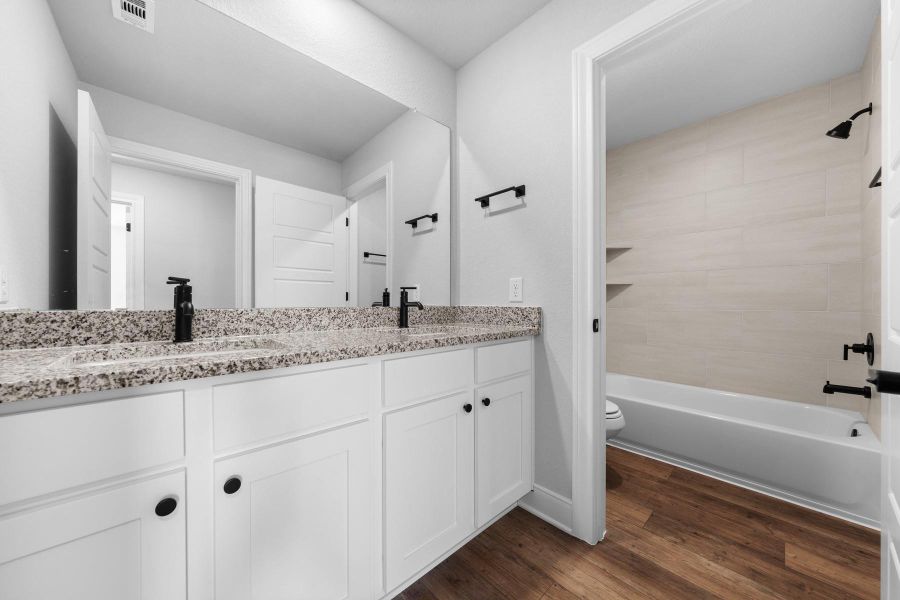 Bathroom featuring double vanity, dark wood-style flooring, and tub / shower combination