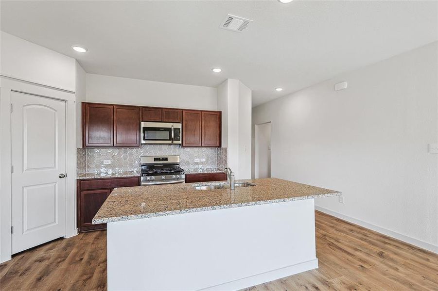 Kitchen with a center island with sink, appliances with stainless steel finishes, sink, and hardwood / wood-style flooring