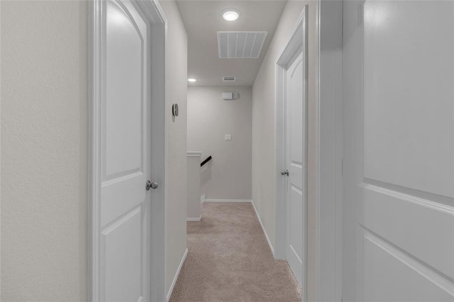 This is a well-lit, neutral-toned hallway featuring plush carpeting, multiple white bedrooms doors, and a clean, modern design.