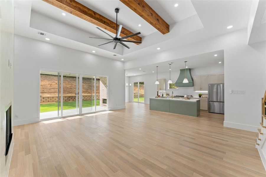 Unfurnished living room featuring beam ceiling, light wood finished floors, ceiling fan, recessed lighting, and a towering ceiling