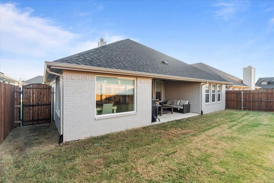 Back of property with brick siding, roof with shingles, a lawn, outdoor lounge area, and a fenced backyard