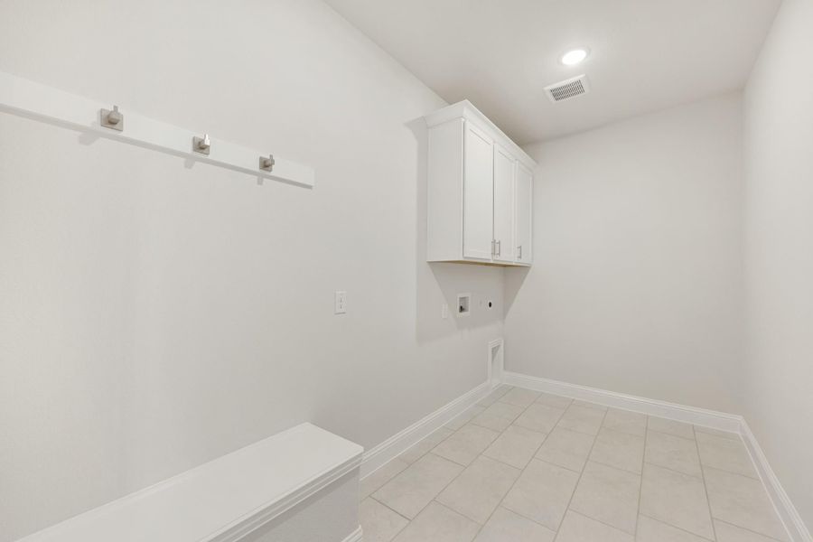 Laundry room with white upper cabinets, wall hooks, built-in bench, and tile floor