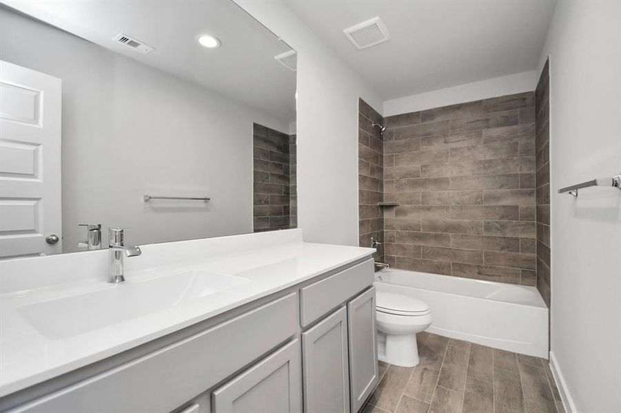 Indulge in refined charm in the secondary bathroom, where the tile flooring harmonizes with a bath/shower combo surrounded by tasteful tile. Light wood cabinets, coupled with a gorgeous countertop, elevate the space, cultivating a truly welcoming atmosphere. Representation of completed home with similar plan. Actual color and selections will vary.