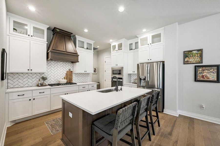 Kitchen with decorative backsplash, appliances with stainless steel finishes, a kitchen bar, custom exhaust hood, and soft close white cabinetry Kitchen with decorative backsplash, appliances with stainless steel finishes, a kitchen bar, custom exhaust hood, and soft close white cabinetry
