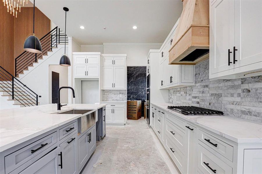 Kitchen with sink, light stone counters, decorative light fixtures, white cabinets, and custom exhaust hood